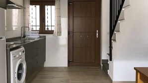 A modern kitchen with a washing machine, wooden beams, a staircase, and a large door. - Alojamiento con terraza en Chulilla (Chulilla)