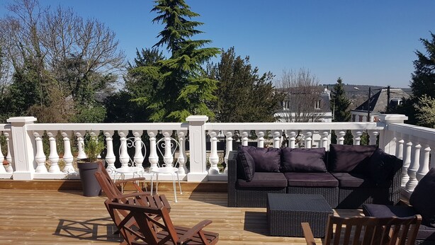 Een houten terras met buitenmeubilair, zoals een bank en stoelen, en een witte balustrade.