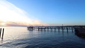 Ein Steg, der sich in ruhiges Wasser erstreckt, mit einem Sonnenuntergang im Hintergrund.