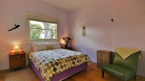 Een slaapkamer met een bed, nachtkastje, stoel, raam en een hangende decoratie.