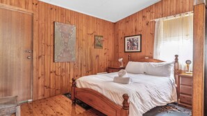 Une chambre à coucher aux murs lambrissés, avec un lit, deux tableaux, une table de chevet et une fenêtre avec des rideaux.
