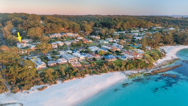 An aerial view of a coastal residential area with houses, a beach, and a forested hill. - Sandals at the Bay - Downstairs, Hyams Beach (Hyams Beach)