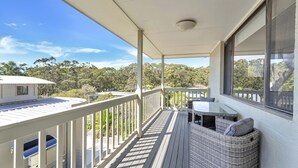 A covered balcony with a table and wicker furniture, overlooking a forested area. - Sandals at the Bay - Upstairs sleeps 6, Hyams Beach (Hyams Beach)