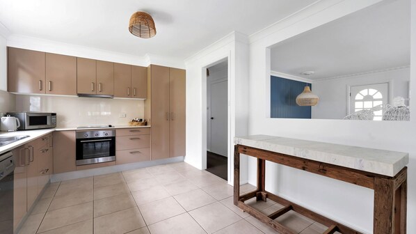 Een moderne keuken met beige kastjes, roestvrijstalen apparatuur en een houten tafel.