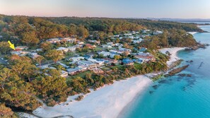 Luchtbeeld van een kustgebied met huizen, een strand en een beboste heuvel.