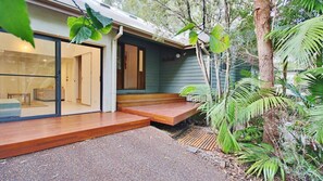 A modern house with a glass door entrance, wooden steps leading to a porch, and a garden with tropical plants. - Sea Mist at Hyams Beach (Hyams Beach)