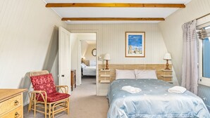A bedroom with a bed, a chair, a bedside table, a lamp, a painting, and a window with curtains. - Sea Point at Hyams Beach (Hyams Beach)
