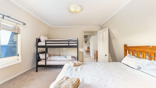 A bedroom with bunk beds, a single bed, a window with blinds, a door, and a ceiling light. - Sea Point at Hyams Beach (Hyams Beach)