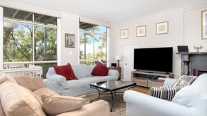 A spacious living room with a large window, a flat-screen TV, and a fireplace. - Sea Point at Hyams Beach (Hyams Beach)