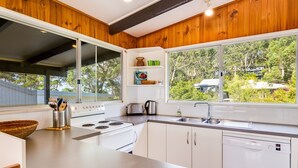 A modern kitchen with white appliances, wooden ceiling beams, and a view of greenery outside. - Shanti at Hyams Beach, Jervis Bay (Hyams Beach)