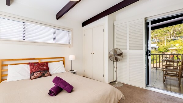 A bedroom with a bed, a fan, a window with blinds, and a view of the outside.