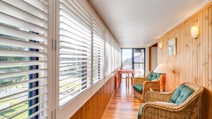 A corridor with wooden flooring, white blinds, wicker furniture, and a small table with chairs. - Shanti at Hyams Beach, Jervis Bay (Hyams Beach)