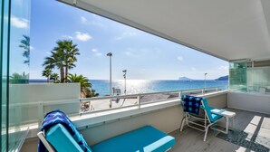 Uma varanda com vista para o mar, uma espreguiçadeira, uma mesinha e um banco.