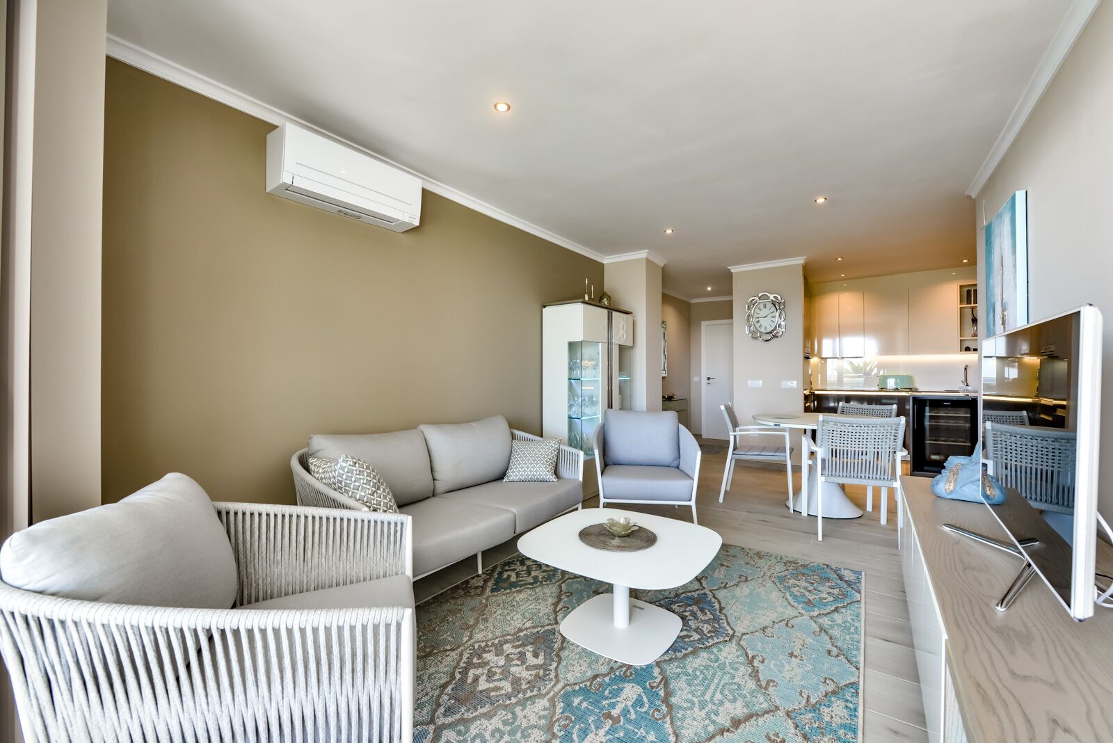 Una sala de estar moderna con un sofá, sillones, una mesa de centro y una zona de cocina con una mesa de comedor y sillas.