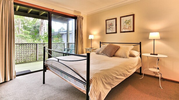 Un dormitorio con cama, dos lámparas de noche, una mesita de noche y un balcón con cortinas.