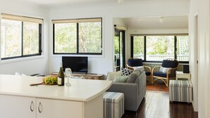 A modern kitchen with a central island, a dining area with a sofa and chairs, and large windows offering a view of greenery.