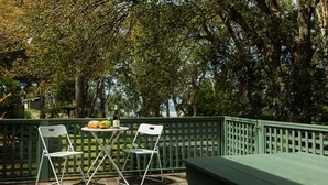 An outdoor seating area with two white chairs and a table, a bottle of wine, and a loaf of bread.
