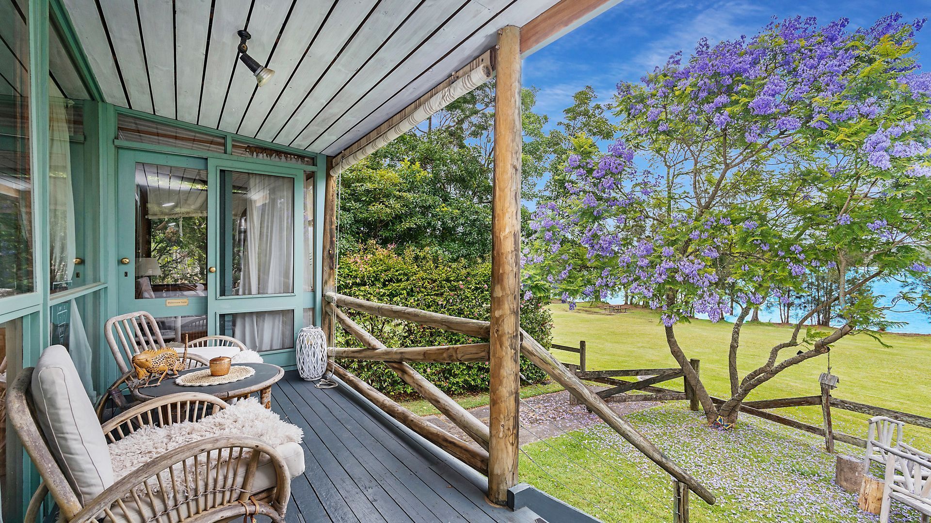 A wooden deck with wicker furniture and a view of purple flowers and a grassy area.