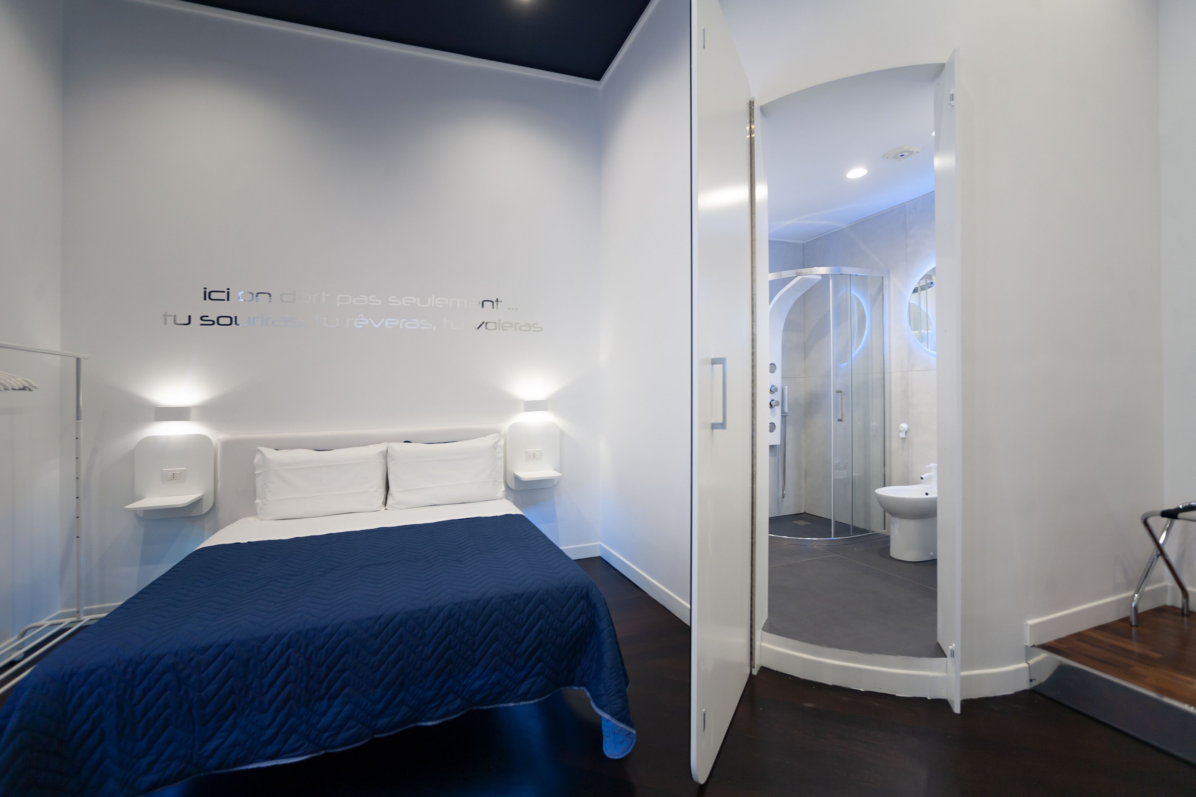 A modern hotel room with a bed, bedside tables, and a bathroom visible through an open door.