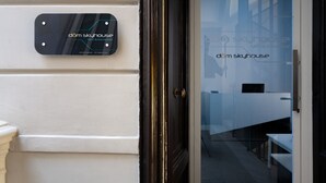 A modern building entrance with a glass door, a sign reading "dam skyhouse bed & breakfast," and a visible interior with a bed and a table. - Skyhouse Duomo (Naples)