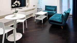 A modern living room with a dark wooden floor, white furniture, a teal sofa, and a TV mounted on the wall. - Skyhouse Duomo (Naples)