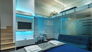 A modern hotel room with a bed, a TV, a desk, and a glass-enclosed bathroom. - Skyhouse Duomo (Naples)
