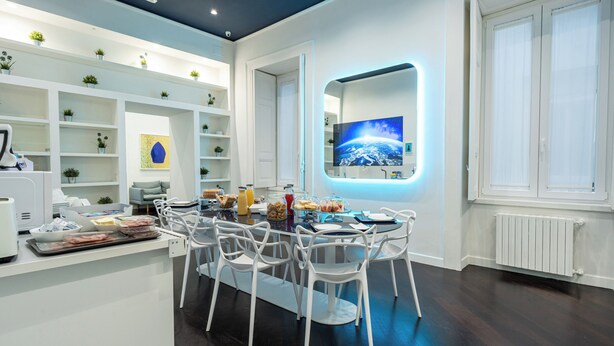 A modern kitchen with white cabinetry, a dining area with white chairs, and a large flat-screen TV mounted on the wall. - Skyhouse Duomo (Naples)