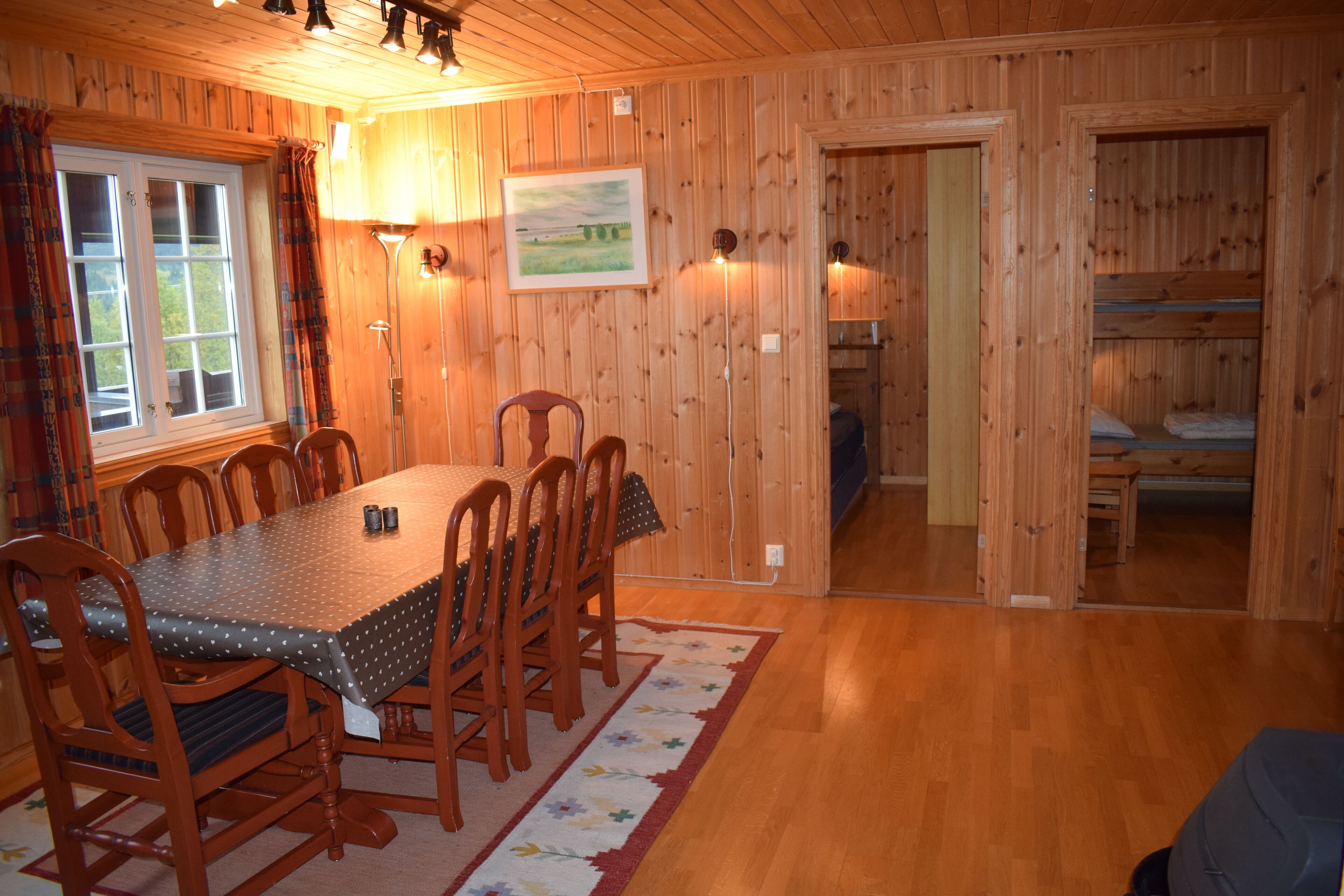 A wooden-paneled room with a dining table, chairs, and a bunk bed.