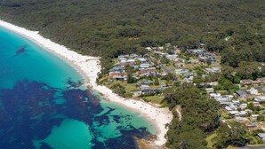 Ett flygbildsbild av ett bostadsområde vid kusten med hus, en strand och ett skogsområde.