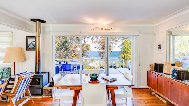 A cozy dining area with a table and chairs, a wooden cabinet, and a view of the outdoors. - The Shack at Palm Beach (Sanctuary Point)