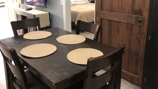 A dining area with a dark wooden table and four chairs, each with a woven placemat. A sliding barn door is visible in the background. - The Cottage at Sunset View Estate.  Close to rafting, hiking, Dollywood 30 mins. (Cosby)