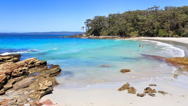 A beach with clear turquoise water, sandy shore, and rocky outcrops.