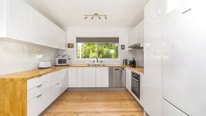 A modern kitchen with white cabinets, a wooden countertop, a built-in oven, and a window with a view of greenery.