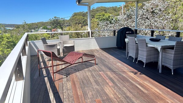 A wooden deck with wicker furniture, a grill, and a view of the landscape.