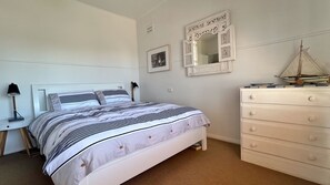 A bedroom with a bed, a dresser, a mirror, and a small sailboat model.