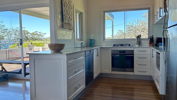 A modern kitchen with white cabinetry, a built-in dishwasher, and a large window offering a view of the outdoors. - Unwind at Hyams Beach, Jervis Bay (Hyams Beach)
