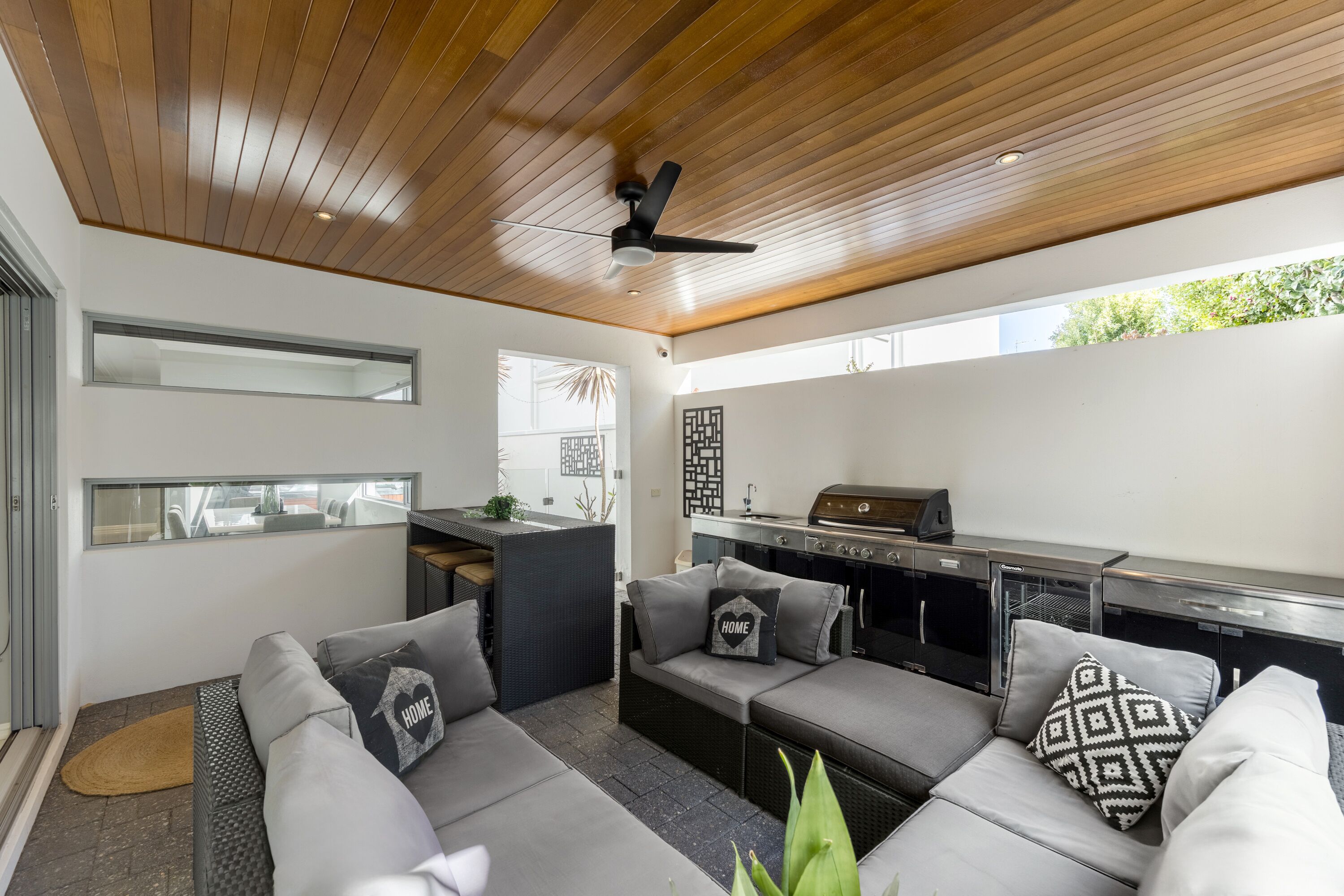Ein modernes Wohnzimmer mit Holzboden, integriertem Grill, grauen Sofas und Blick ins Freie.