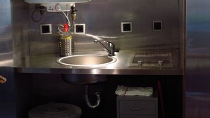 A stainless steel kitchen with a sink, a faucet, and a water heater. There are small cabinets and a drawer below the sink. - Room in Cabin - Restored, Rustic and Rural Mini Cottage in Typical Portuguese Village (Lamego)