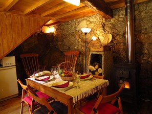 A cozy dining area with a stone wall, wooden ceiling beams, and a wood-burning stove. - Room in Cabin - Restored, Rustic and Rural Mini Cottage in Typical Portuguese Village (Lamego)