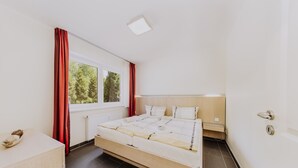 Un dormitorio moderno con una cama grande, cabecero de madera, una mesita de noche y una ventana con cortinas.