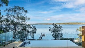 Piscina moderna com barreira de vidro, cercada por árvores e vista para um lago tranquilo.