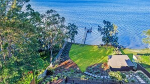 Um jardim ajardinado com um deck de madeira, gramado e vista para o mar.
