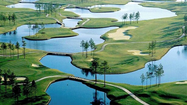 Een golfbaan met waterhindernissen, zandbunkers en een brug.