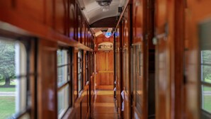 A narrow corridor with wooden paneling and large windows on both sides, leading to a central area with a ceiling fan and a sign indicating a ladies' section.