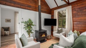 A cozy living room with a wood-burning stove, striped sofas, a television, and a large window with curtains.