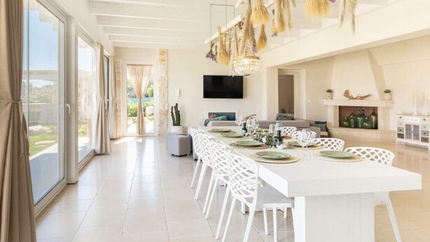 Een ruime eetruimte met een lange witte tafel, witte stoelen en een kroonluchter met decoraties.