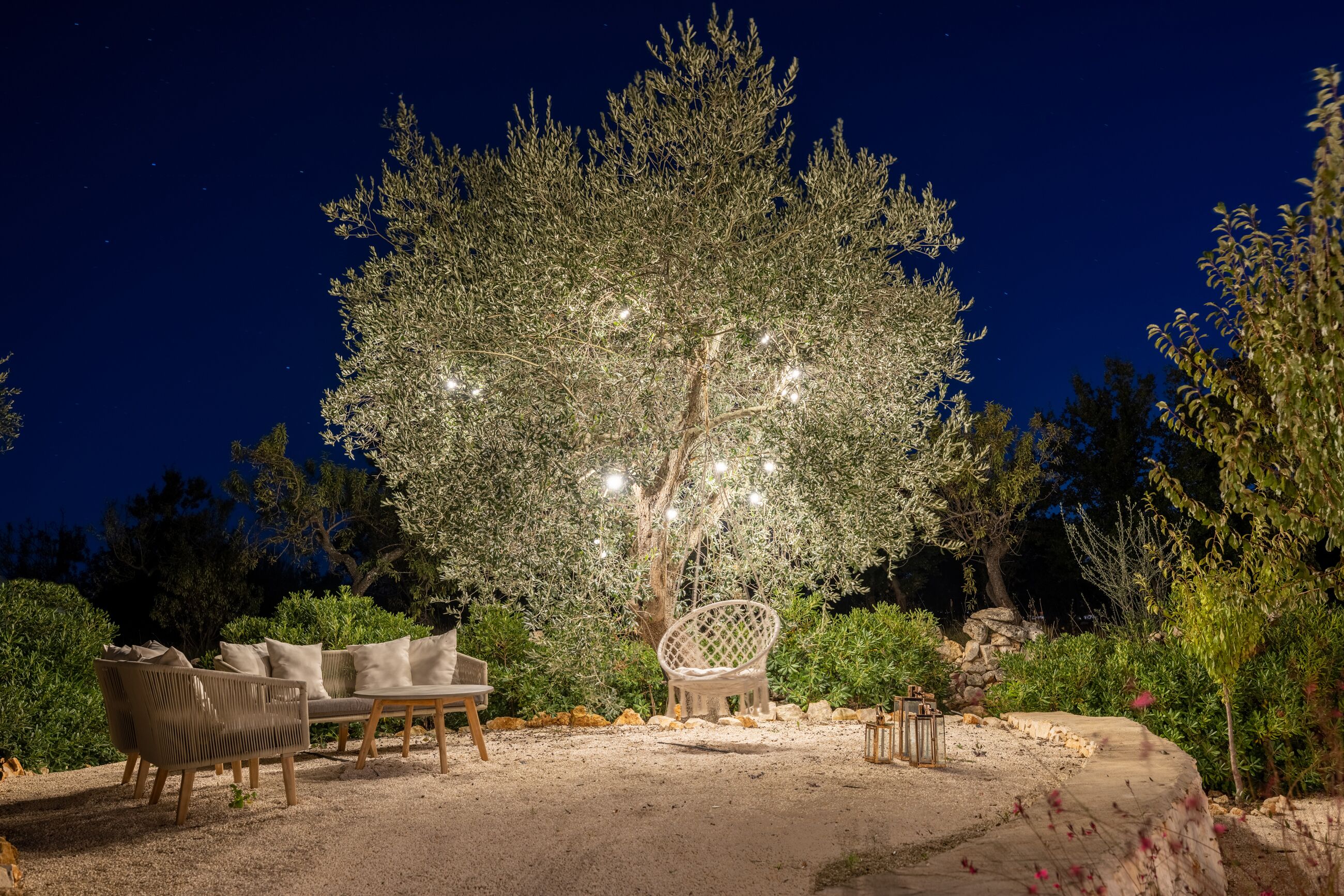 Un espace extérieur aménagé avec des meubles en osier et un arbre décoratif illuminé, le tout entouré de verdure.