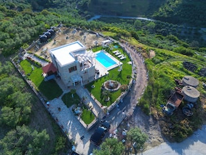 An aerial view of a property with a swimming pool, stone patio, and surrounding greenery.