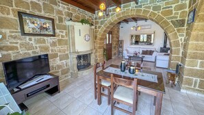 A stone-walled living room with a fireplace, a television, and a dining area with a table and chairs. - Traditional Fully Private Villa with Pool (Chania)