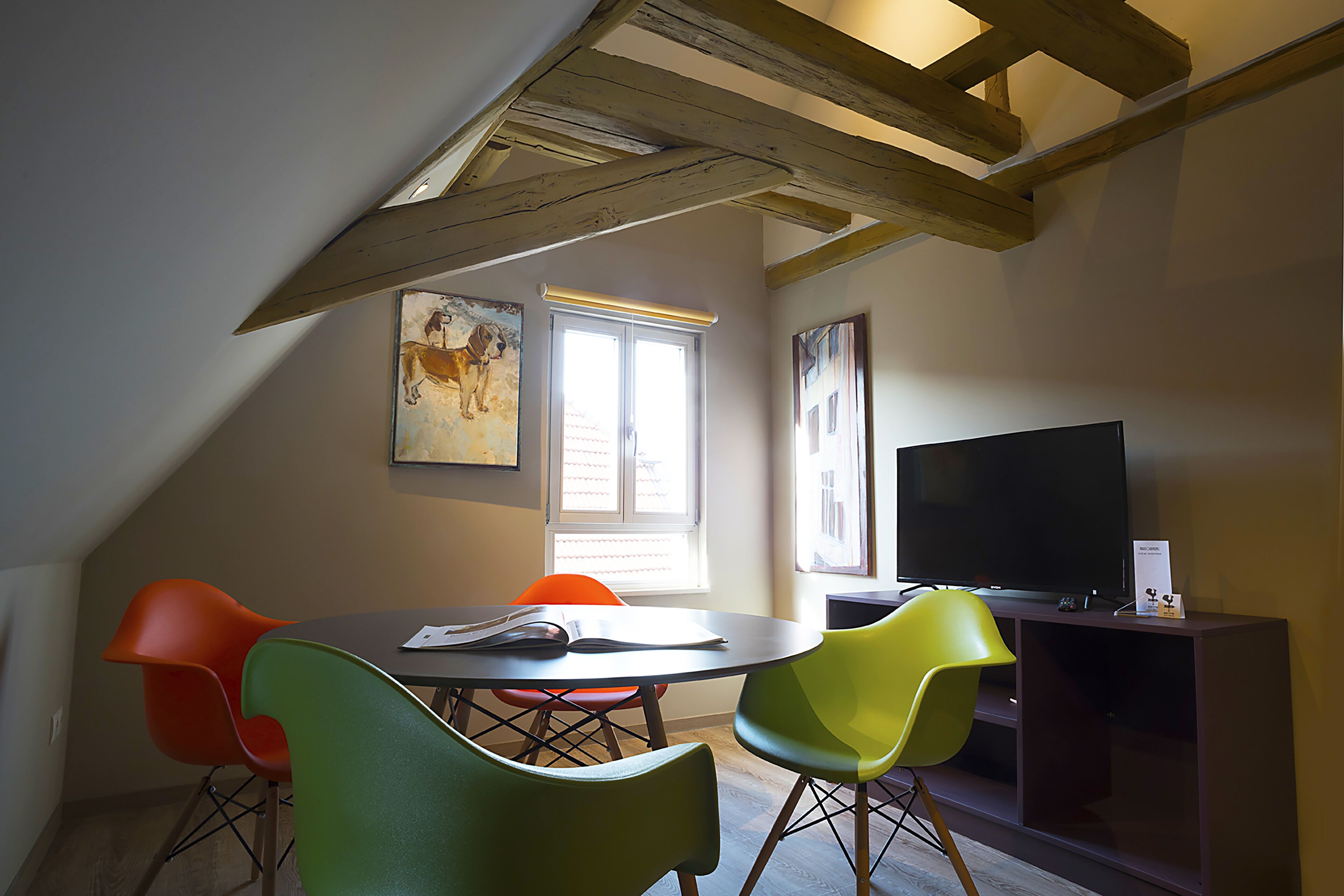 A dining area with a round table, four chairs, a television, and artwork on the walls.